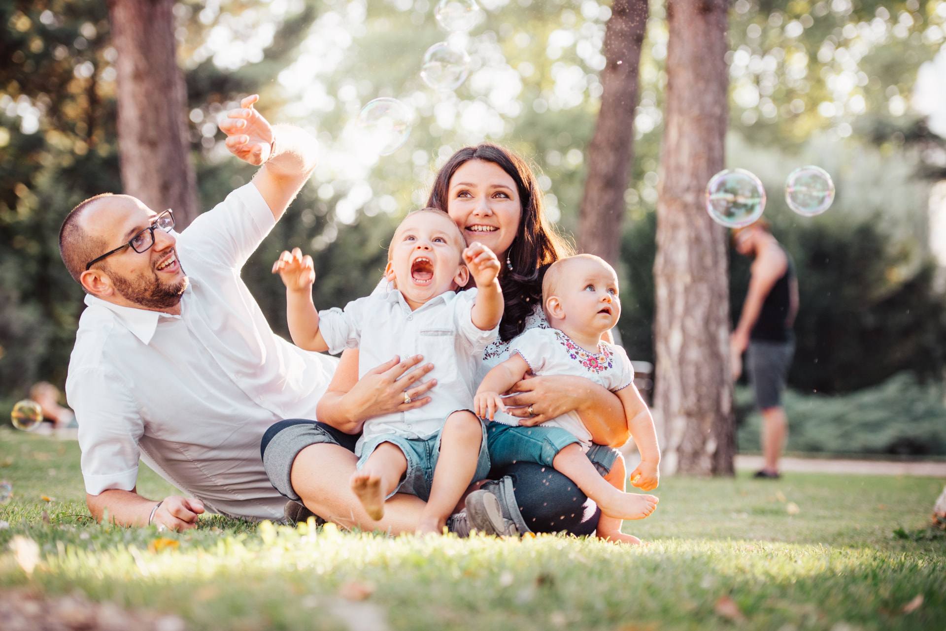 A young family playing with bubbles together in a sunlit park